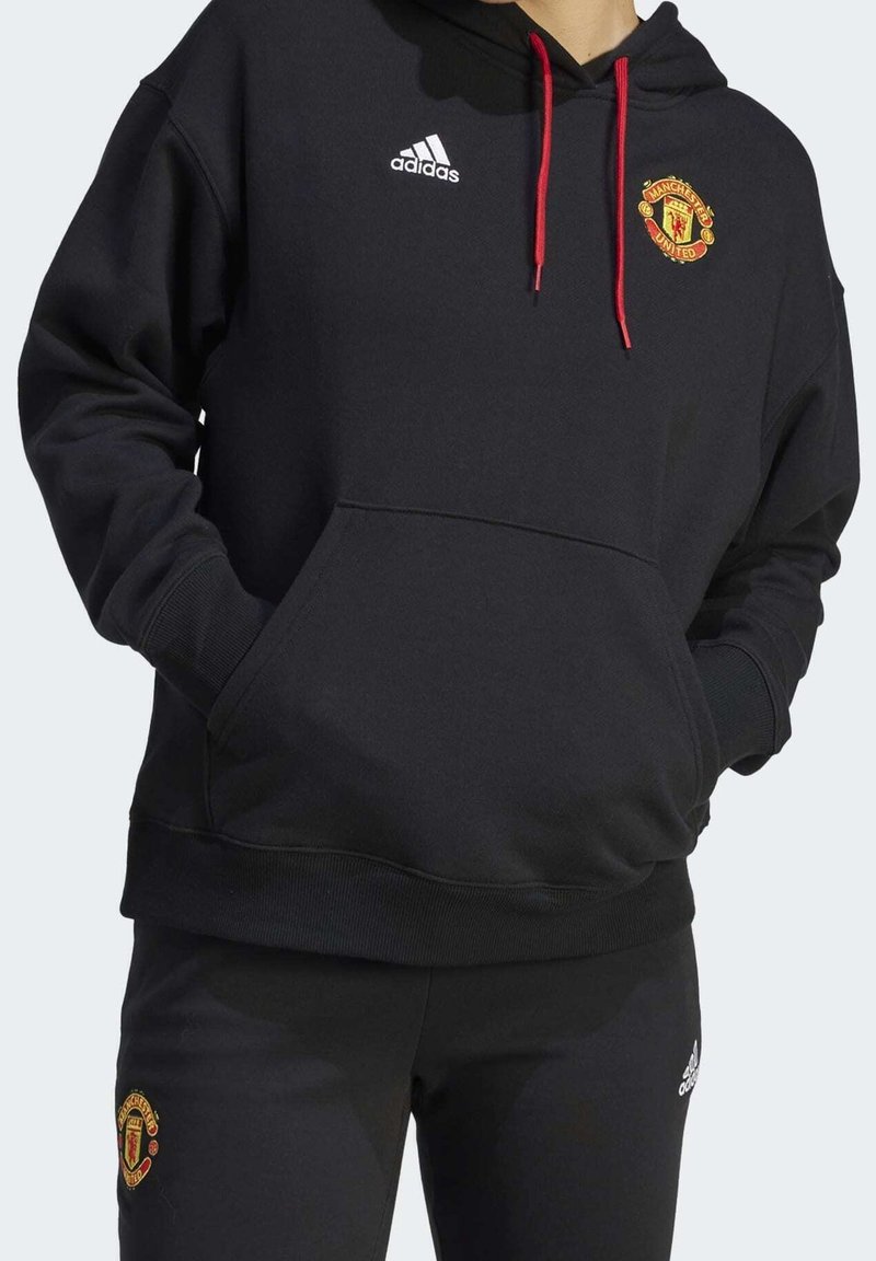 Sweat à capuche en mélange de coton noir avec une poche avant, des cordons rouges, et un logo Adidas blanc accompagné d'un emblème de Manchester United sur la poitrine.