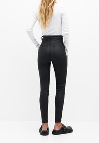 Pantalon noir taille haute en matière extensible, avec deux poches arrière et une texture lisse. Associé à des sandales plates noires.