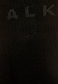 Calcetín negro de punto con textura acanalada y diseño de logo sutil. Presenta un acabado suave y secciones reforzadas en el talón y la puntera.