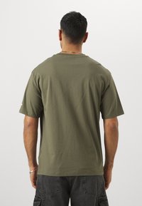 Oliven grøn bomulds t-shirt med en afslappet pasform. Korte ærmer og rund halsudskæring, vist fra ryggen, med en glat tekstur.
