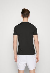 Camiseta negra de manga corta fabricada en tejido suave, con cuello redondo y un diseño ajustado, vista desde la parte trasera.