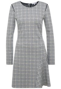 Vestido de manga larga hasta la rodilla con un patrón a cuadros en blanco y negro y líneas beige sutiles, que presenta un escote redondo y un dobladillo asimétrico.