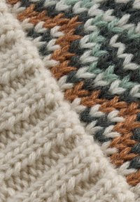 Tissu tricoté présentant deux textures : un beige crémeux avec un tissage épais et une section à motifs multicolores aux tonalités terreuses et aux verts doux.