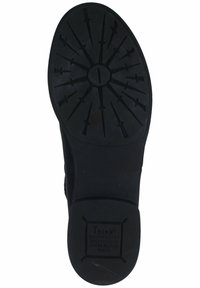 Suela de goma negra con un dibujo en relieve con flechas, forma redondeada y detalles de marca en relieve. Textura suave con un diseño robusto.