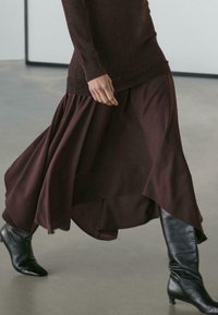 Dlouhá bordó sukně s plynulým střihem, v kombinaci s elegantními černými koženými kozačkami ke kolenům. Hladká textura látky a vrstvený lem.