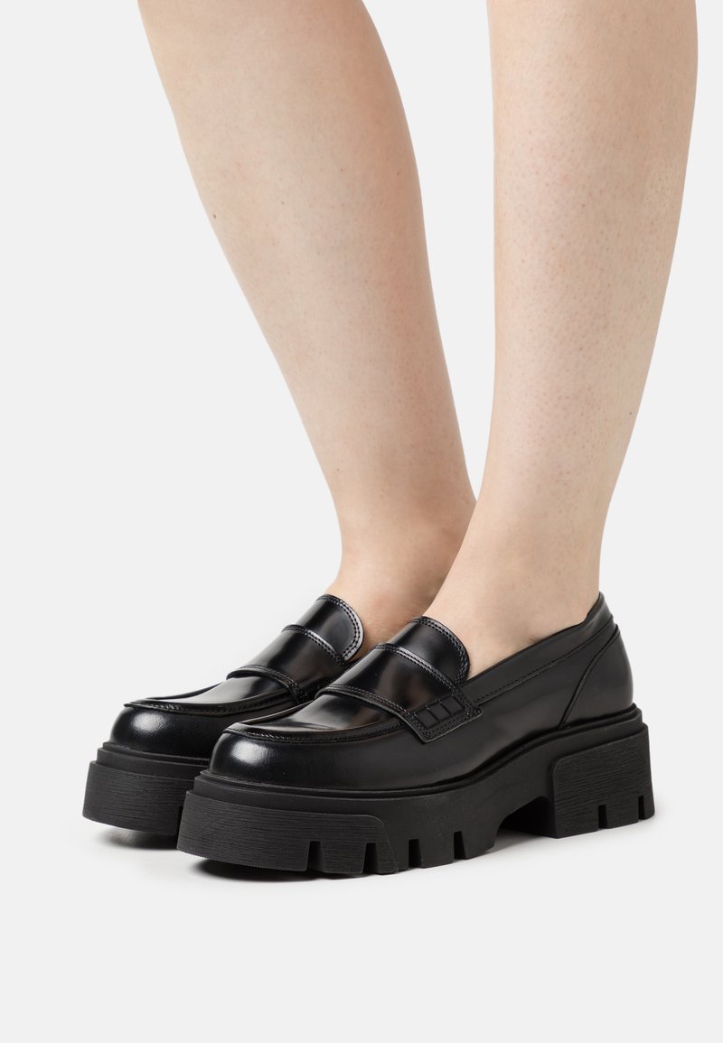 Mocassini in pelle nera con suola platform chunky, caratterizzati da una finitura liscia e un delicato dettaglio di cucitura sulla parte superiore.