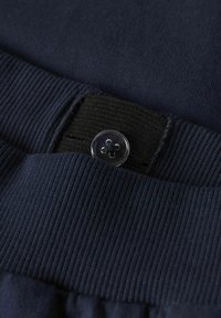 Détail en tissu marine avec une texture côtelée à la taille, doté d'un bandeau élastique noir et d'un bouton transparent à quatre trous.
