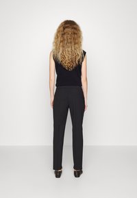 Svart ärmlös topp som matchas med slim-fit svarta byxor. Tyget verkar mjukt med en subtil lyster. Enkel design, minimala synliga detaljer.