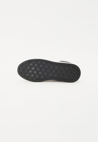 Fekete sneaker talp, textúrált gumifelülettel, barázdás mintázattal, lapos formával és gravírozott logó részletekkel.