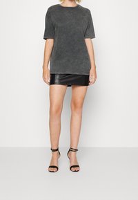 Tmavě šedé oversized tričko z měkkého texturovaného materiálu, spárované s vypasovanou černou mini sukní z umělé kůže a černými sandály na řemínky.