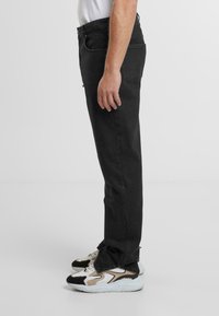 Jeans din denim negru cu o croială dreaptă, având buzunare standard și o suprafață texturată, asortați cu teniși chunky negri și albi.