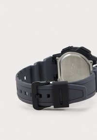 Montre en caoutchouc grise avec un bracelet texturé, dotée d'une boucle noire, d'un fond en métal et d'un design robuste adapté à une utilisation en extérieur.
