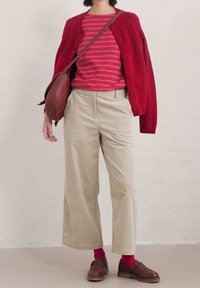 Röd stickad cardigan över en rosa randig skjorta, tillsammans med beige vida kordflossbyxor. Bruna loafers och rosa strumpor fulländar looken.