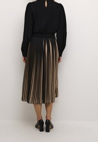 Svart långärmad topp med knäppningar vid ärmarna, kombinerad med en plisserad midikjol med vertikala svarta och beige ränder. Svarta klackskor.