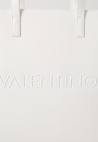 Fehér, dombornyomott anyagból készült táska, amelyen a "VALENTINO" szó jól látható, fényes fehér betűkkel szerepel.