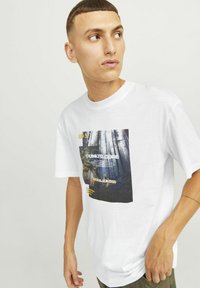 Hvid bomulds T-shirt med et centralt grafisk print af træer med tekst i sort og gul. Korte ærmer og en afslappet pasform.