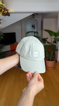 Casquette gris clair à forme structurée, avec un logo carré à l'avant et des trous de ventilation. Semble fabriquée en tissu texturé.