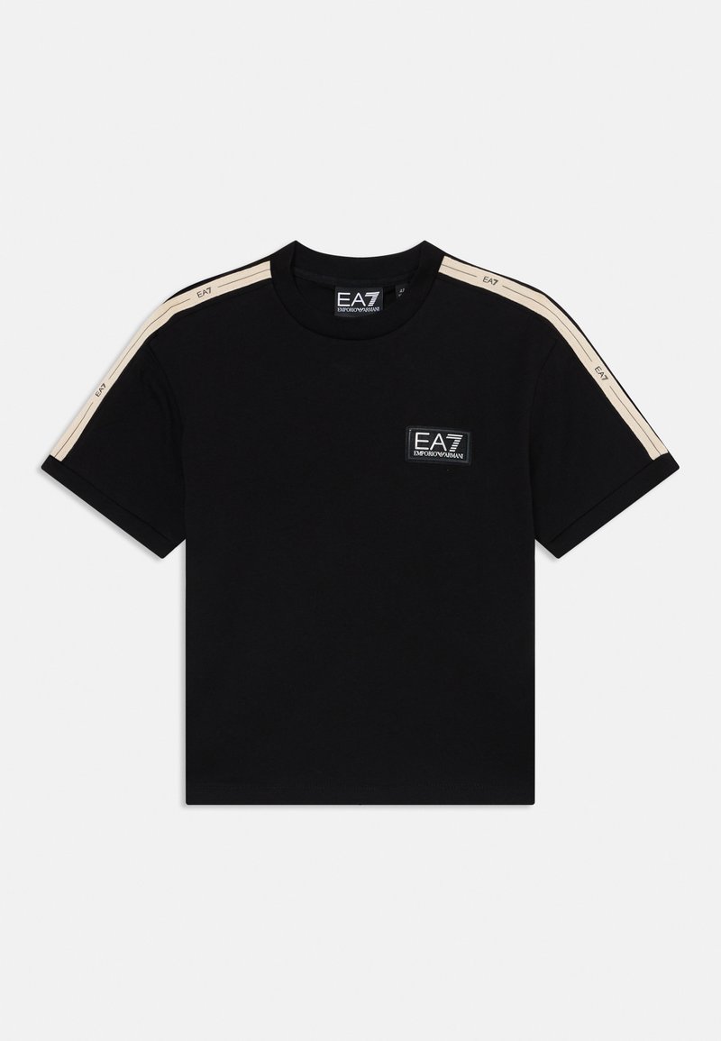 T-shirt de algodão preta com mangas curtas, apresentando riscas bege nos ombros e um pequeno patch do logo EA7 no peito. Textura suave.