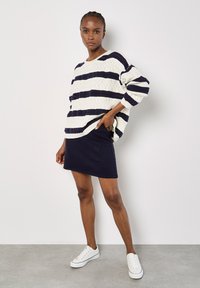 Gestreifter Pullover in Marineblau und Creme mit strukturiertem Stoff; kombiniert mit einem figurbetonten Marineblauen Rock und weißen Turnschuhen.
