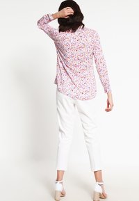 Blomstret langærmet skjorte med en pink bund, der har små flerfarvede mønstre. Sammen med hvide bukser og lyse block heels.
