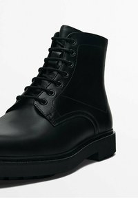Stivaletti in pelle nera con punta arrotondata, allacciatura frontale e finitura texturizzata. Suola in gomma resistente con design basso e piatto.