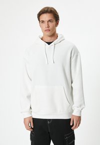 Felpa bianca con cappuccio, tasca frontale, coulisse e vestibilità rilassata. Caratterizzata da polsini e orlo a coste, abbinata a pantaloni cargo neri.