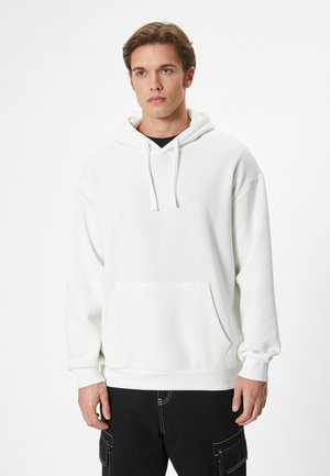Hvid pullover hoodie med en frontlomme, snøre i hætten og en afslappet pasform. Har ribbede mansjetter og kant, parret med sorte cargo bukser.