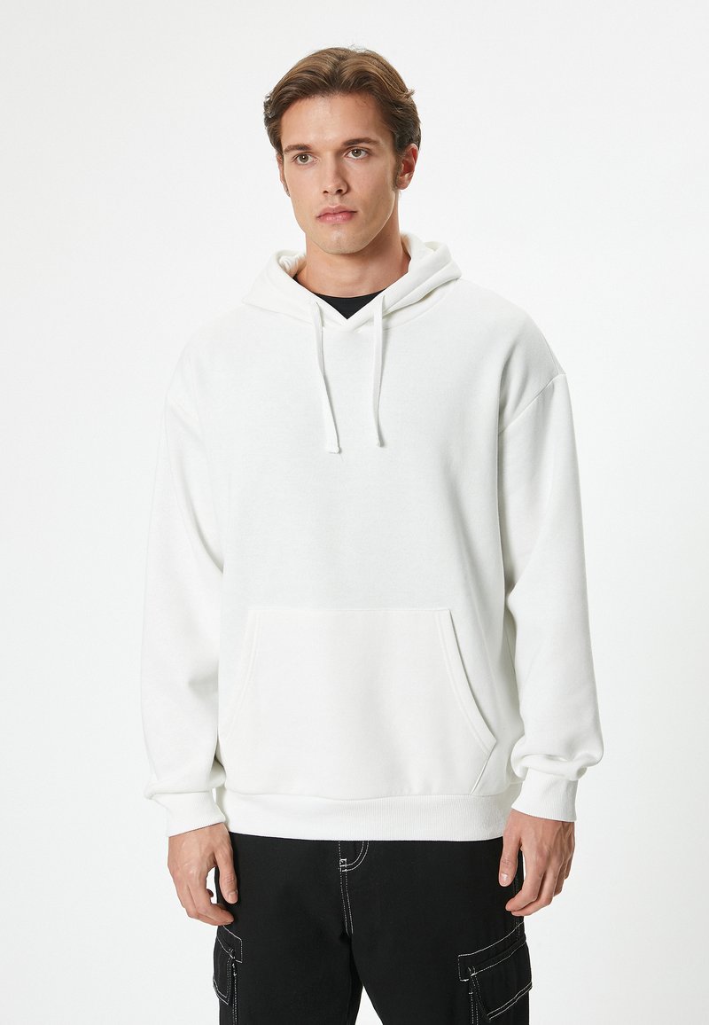 Weißer Pullover-Hoodie mit Kängurutasche, Kordelzugkapuze und lässiger Passform. Mit gerippten Bündchen und Saum, kombiniert mit schwarzen Cargo-Hosen.