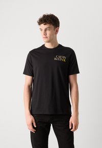 Sort bomulds t-shirt med rund hals og korte ærmer. Lille guld- og hvidt "CALVIN KLEIN" logo på den øverste venstre bryst.