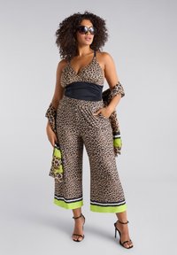 Leopardmönstrad jumpsuit med svart liv och åtdragen midja. Har vida, korta ben och en limegrön detalj vid fållen. Svarta sandaler.