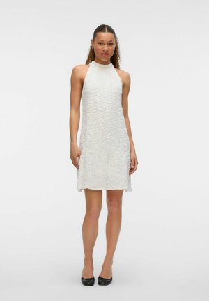 White halter neck dress with textured pattern, featuring a slightly flared hem and a smooth finish. Worn with black flats.