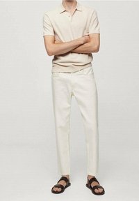 Beżowa koszulka polo, białe slim-fit dżinsy i brązowe sandały. Koszulka ma krótki rękaw; dżinsy mają standardowy projekt czterech kieszeni.