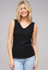 Zwarte mouwloze top met een V-halsontwerp, gemaakt van gestructureerde stof met geometrische uitsparingen, gecombineerd met lichtblauwe jeans.