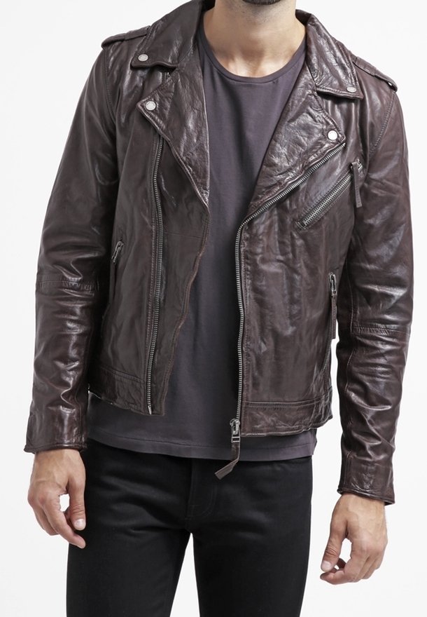 Giacca da moto in pelle marrone con zipper asimmetrico sul davanti, spalline e numerose tasche con zip. Indossata sopra una camicia scura.