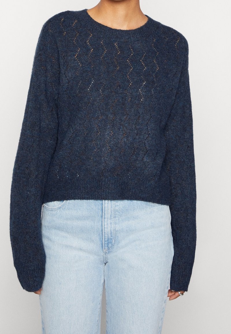 Pull en tricot bleu marine avec un motif zigzag texturé, col rond et manches longues, associé à un jean taille haute bleu clair.