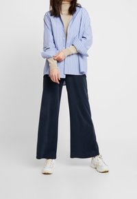 Modrá a bílá pruhovaná oversize košile s knoflíkovým zapínáním, zkombinovaná s volnými námořnickými širok ými kalhotami a bílými teniskami. Hladká bavlněná látka.