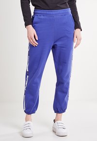 Blauwe katoenen joggers met een elastische tailleband en manchetten, met witte zijstrepen en logoaccenten. Glad textuur en taps toelopende pasvorm.