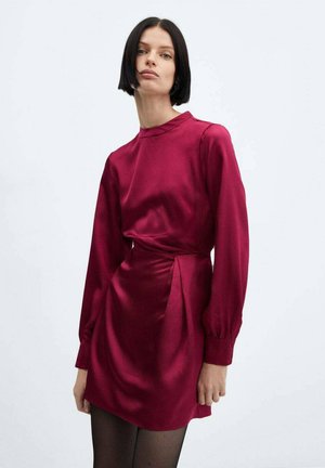 Short long-sleeve dress, deep burgundy satin fabric, smooth texture, with a high neck and draped waist detail. Black tights worn.