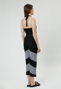 Zwart-witte gestreepte jumpsuit met halternek, aansluitende bovenkant en wijde broekspijpen met diagonale streeppatroon. Inclusief platte sandalen.
