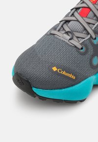 Chaussure de sport grise avec une tige texturée et une semelle turquoise. Comprend des lacets gris, un accent rouge et un logo Columbia visible en orange.