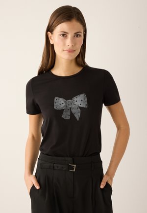 Black T-shirt with a silvery polka-dotted bow graphic on the front. Short sleeves and a classic round neckline. Smooth texture.