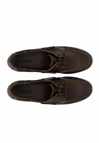 Paire de chaussures bateau en cuir marron foncé avec des coutures claires et des lacets noirs, vue de dessus sur un fond blanc.