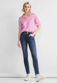 Camisa de manga larga a rayas rosas y blancas, combinada con jeans skinny azul oscuro y zapatillas claras, con un corte ajustado y puños doblados.