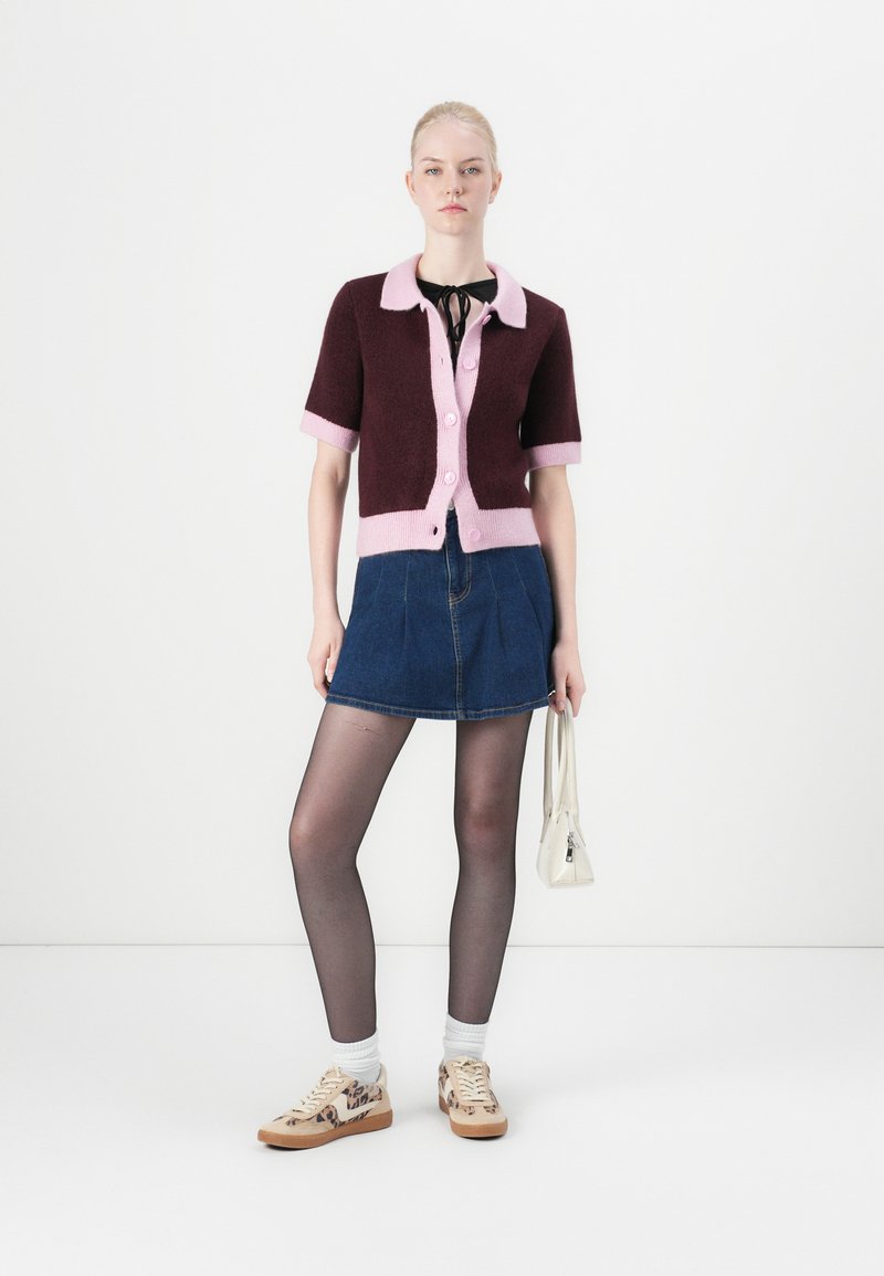 Bordeaux en roze kortemouwe cardigan, knoopsluiting aan de voorkant; denim mini rok; transparante zwarte panty; gemusterde sneakers; kleine witte handtas.