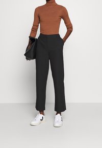 Col roulé côtelé marron, pantalons noirs taille haute et baskets blanches avec des accents noirs. Design épuré et coupe ajustée.