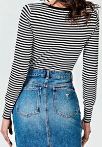 Top de manga larga a rayas blanco y negro combinado con una falda lápiz de mezclilla azul que cuenta con dos bolsillos traseros y un acento de logo triangular.