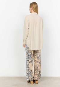 Beige Langarmshirt mit Rückenpasse, kombiniert mit gemusterten, weit geschnittenen Hosen in Grau-, Schwarz- und Beige-Tönen. Sandalen mit Korkabsatz.