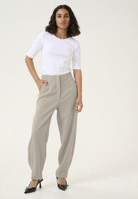 Wit geribbeld topje met korte mouwen, gecombineerd met hooggetailleerde beige wijde broek en zwarte hoge hakken met een puntige neus en details.