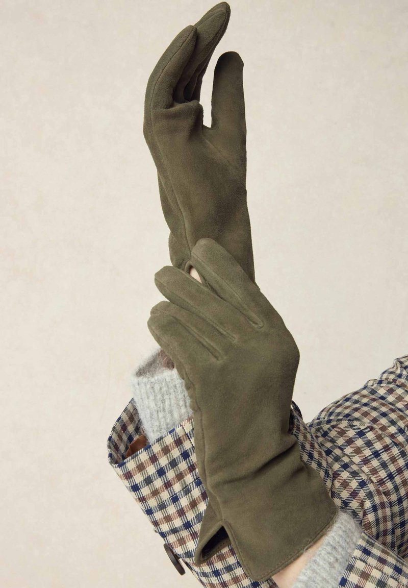 Olive green gloves made of soft suede, featuring a snug fit and elegant design. The accenting outfit has a checkered pattern.