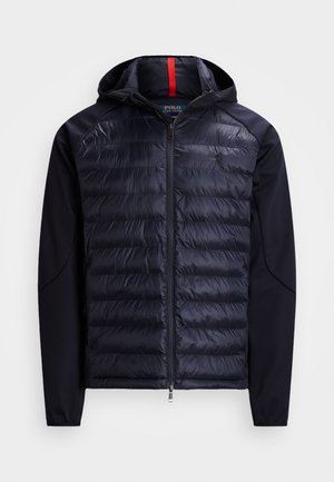 Granatowa kurtka puchowa z kapturem, z pikowaną przednią częścią, bezszwowymi rękawami i zamkiem błyskawicznym. Czerwony akcent wewnątrz kaptura.